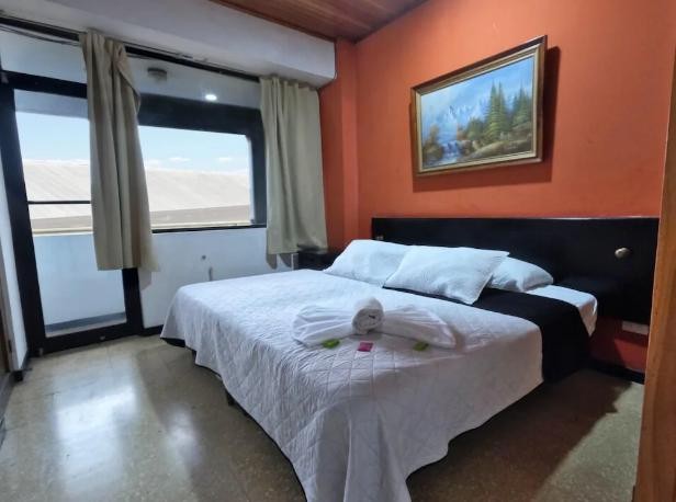 Habitación con pared naranja, cama matrimonial y ventanal