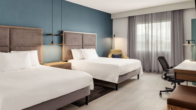 Habitación con dos camas dobles, pared azul, escritorio y silla de trabajo