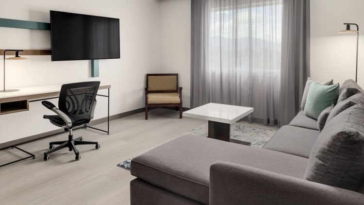 Sala de una suite con sofá seccional, escritorio, televisor y ventanal a las montañas