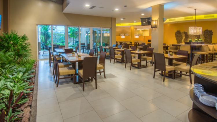 Restaurante con mesas de madera y ventanales corredizos hacia un patio con plantas