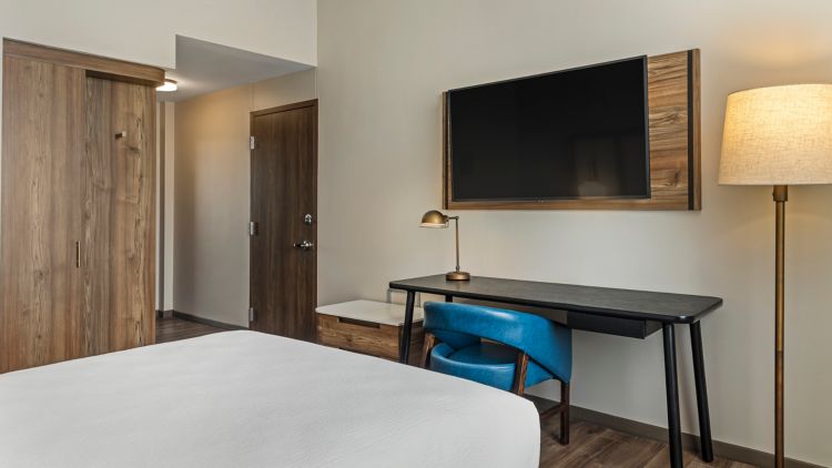 Habitación con cama, escritorio, silla azul y televisor sobre panel de madera