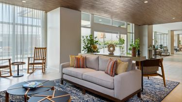 Sala del lobby con sofá, mesas bajas y ventanales hacia un jardín interior