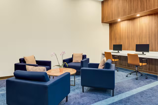 Sala de trabajo con sillones azules y dos puestos de computadora sobre un mueble de madera
