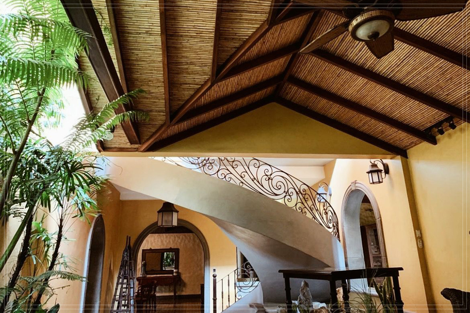 Atrio del hotel con techo de caña, escalera curva y barandal de hierro forjado